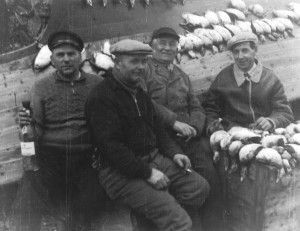 Fyra män sitter bland skjutna fåglar